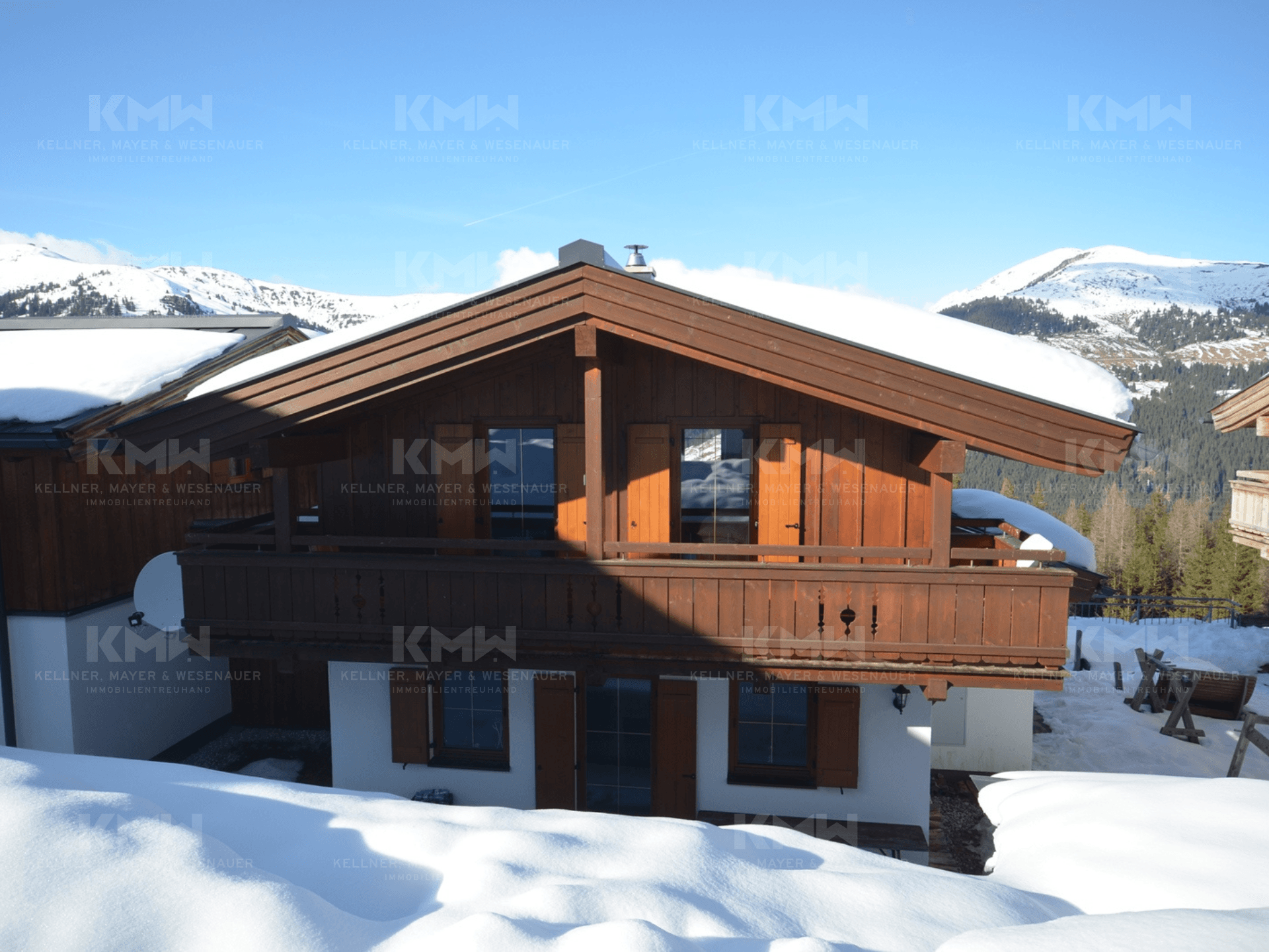 Traditionelles Holzchalet mit Satteldach, Balkonen und verschneiter Umgebung in den Bergen.
