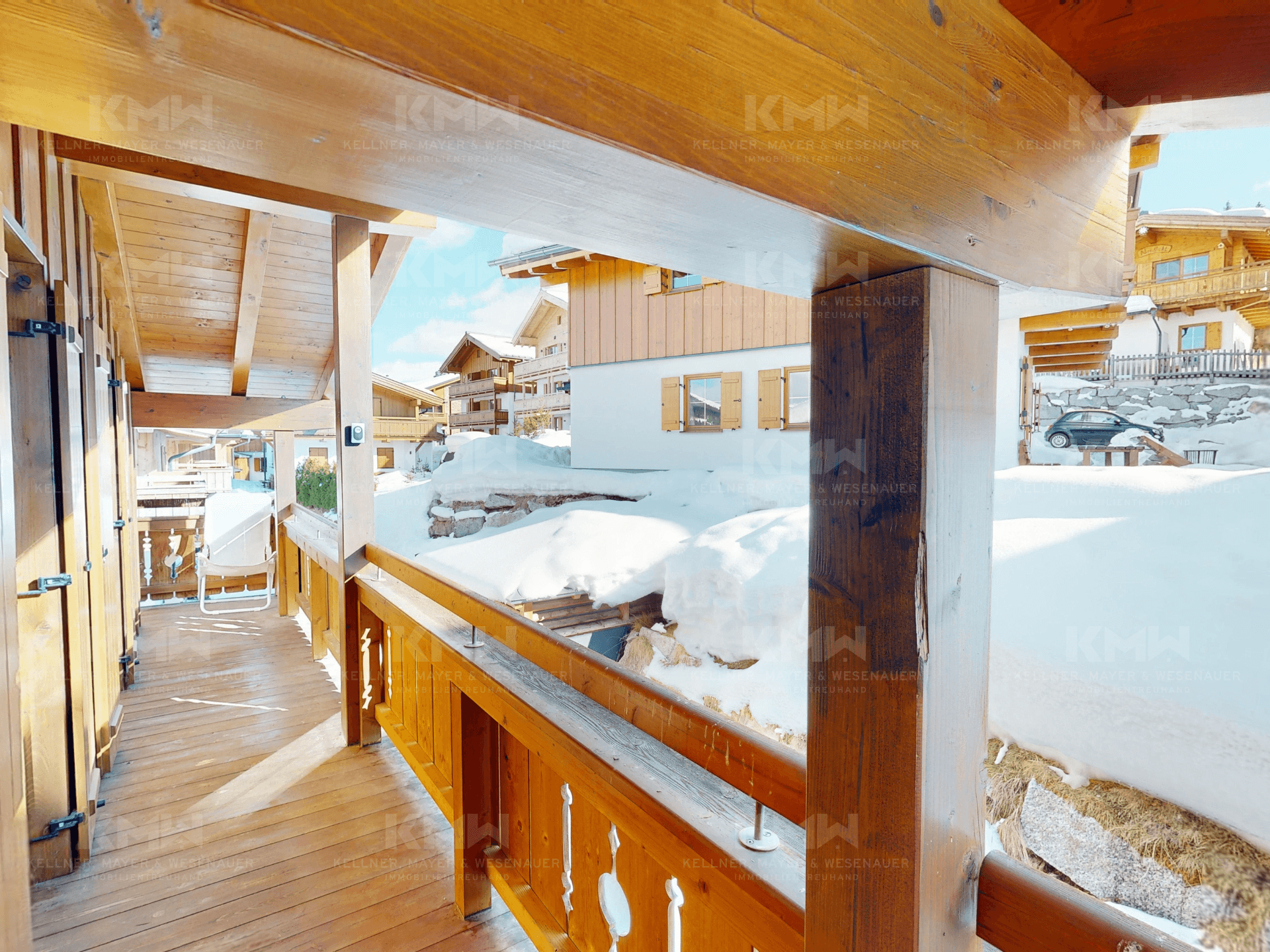 Überdachter Holzbalkon mit Blick auf die verschneite Umgebung und benachbarte Chalets.