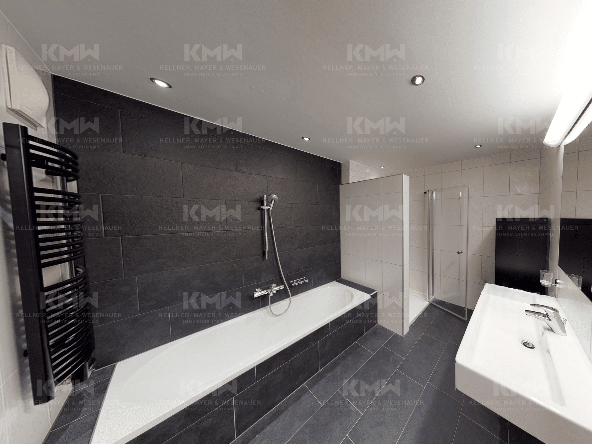 Elegantes Badezimmer mit Badewanne, Duschbereich und dunklen Wand- und Bodenfliesen.
