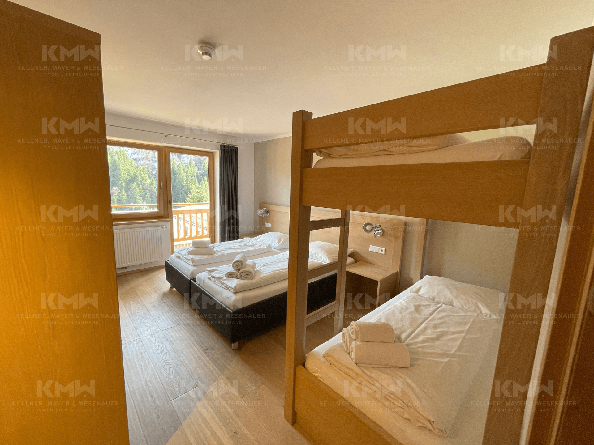 Helles Schlafzimmer mit Doppelbett, Etagenbett und Holzboden, mit Blick ins Grüne.