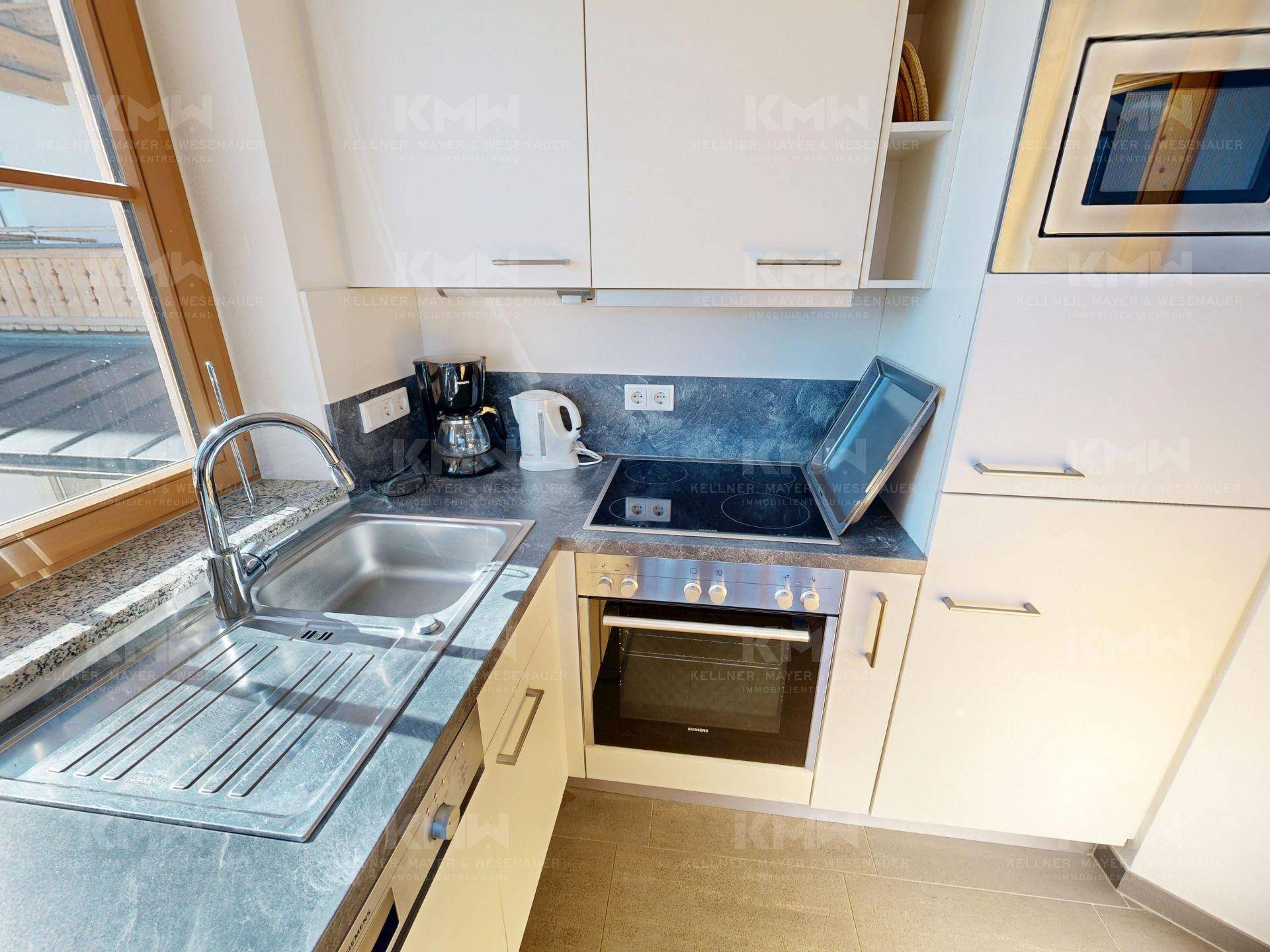 Funktionale Küchenzeile mit Spüle, Kochfeld, Backofen und Mikrowelle in hellem Design.