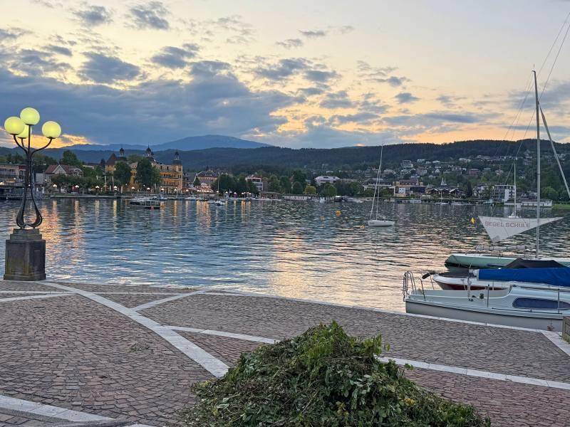 Abendstimmung am See mit Booten, Uferpromenade und Bergen im Hintergrund.
