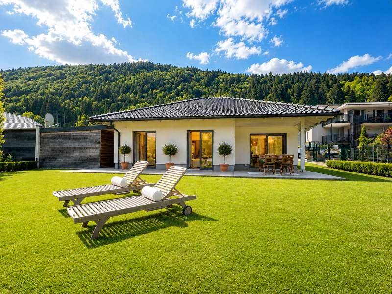 Großzügiger Gartenbereich mit Liegestühlen und modernem Haus vor bewaldeter Bergkulisse.