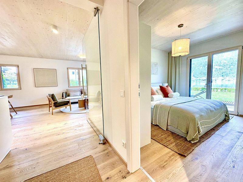 Schlafzimmer mit Holzboden und Zugang zur Terrasse, verbunden mit dem Wohnbereich durch Glas.