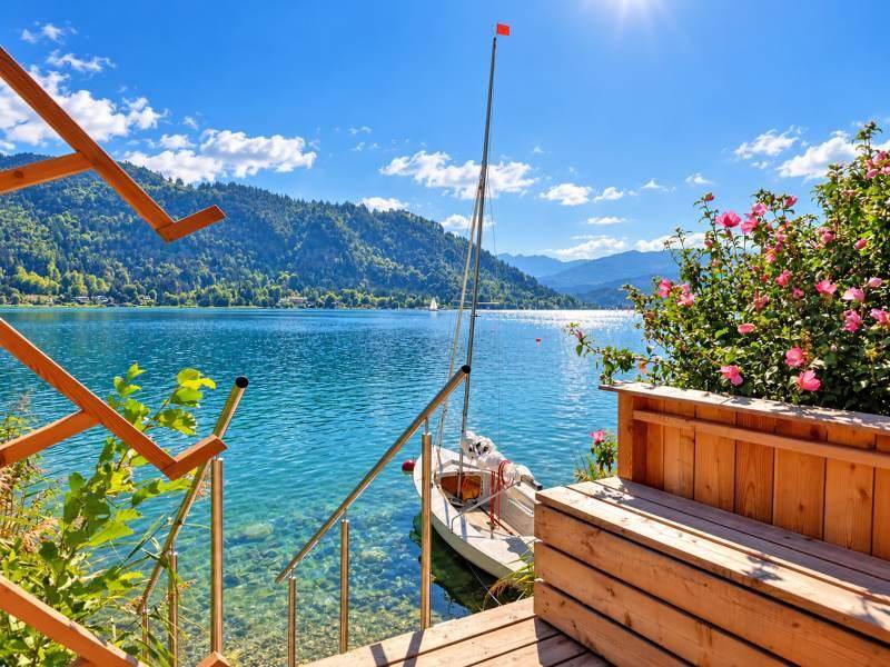 Holztreppe führt direkt zum klaren Seeufer mit einem kleinen Boot und blühenden Rosen.