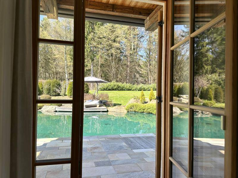Blick durch die offene Holztür auf den einladenden Poolbereich und den gepflegten Garten.