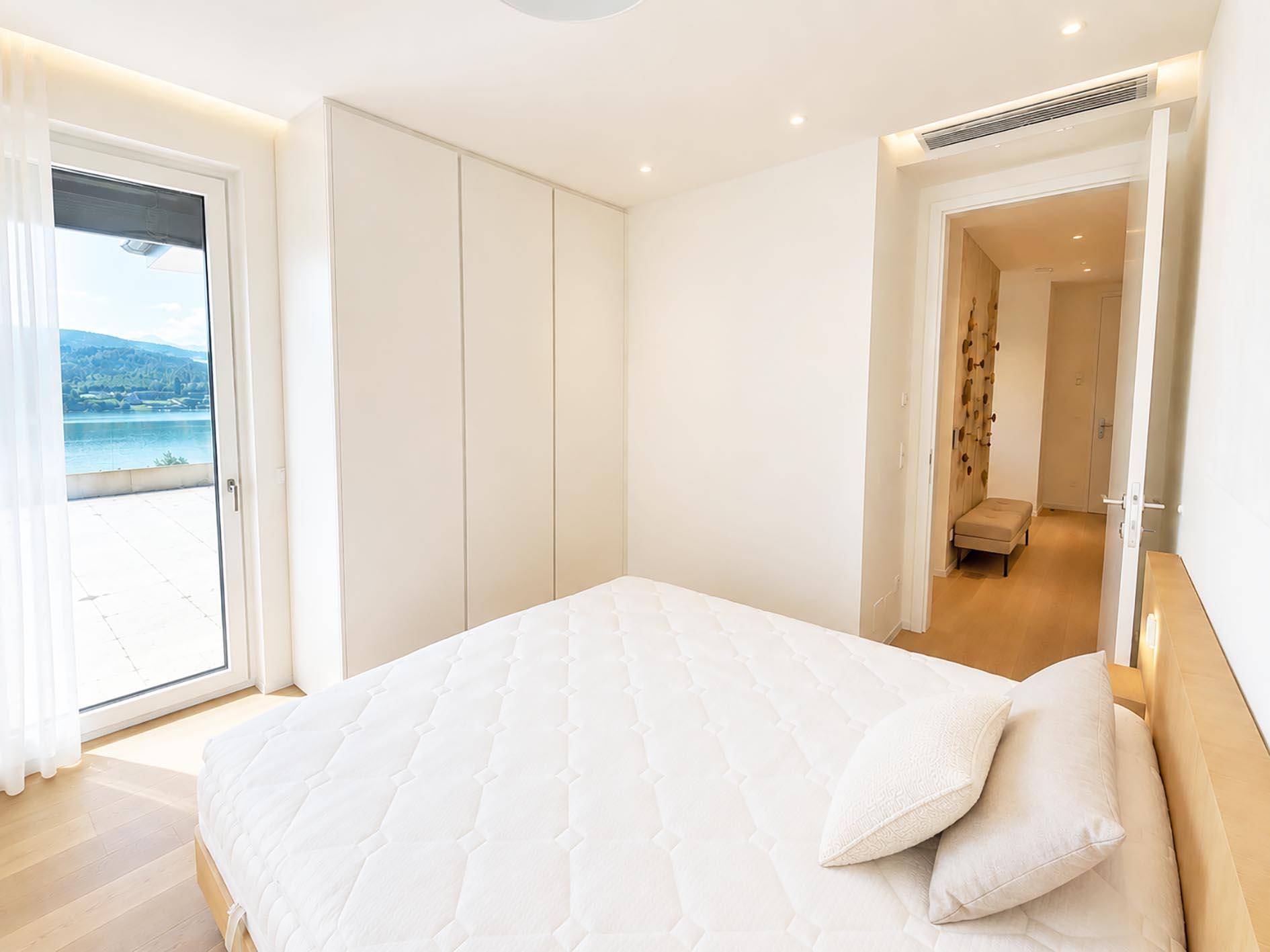 Geräumiges Schlafzimmer mit Einbauschränken, Holzboden und Zugang zu einer Terrasse mit Seeblick.