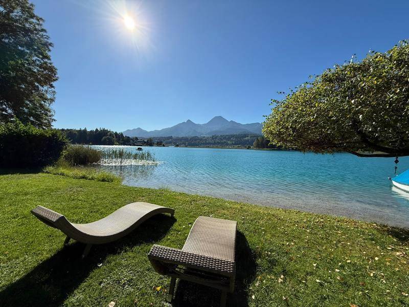 Sonniger Gartenbereich am Seeufer mit bequemen Liegestühlen und beeindruckendem Bergpanorama im Hintergrund.