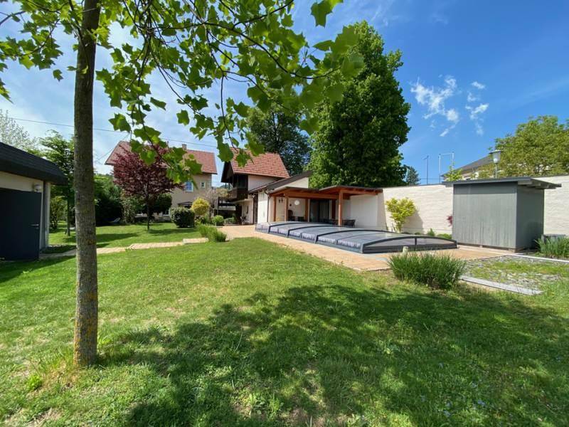 Gepflegter Garten mit abgedecktem Pool und altem Baumbestand unter blauem Himmel.