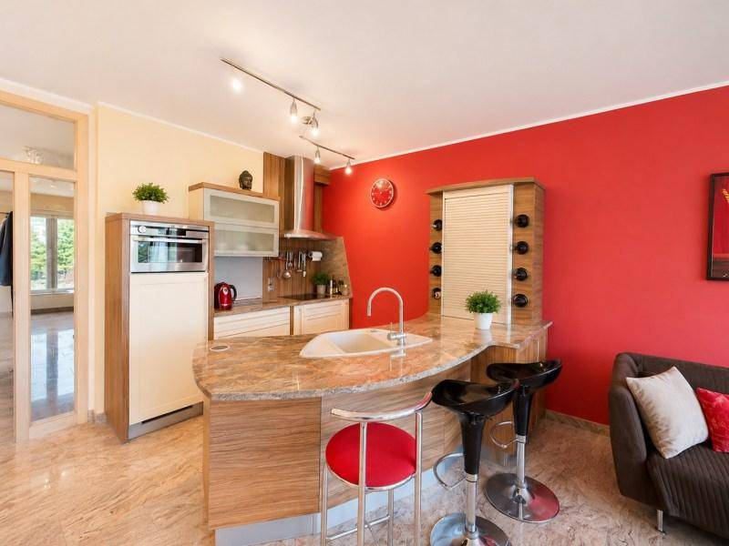 Moderne offene Küche mit Kücheninsel, Barhockern und roter Akzentwand.