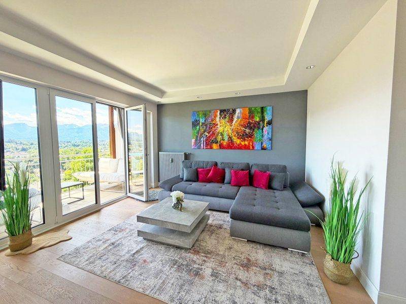 Helles Wohnzimmer mit großem Ecksofa, modernem Couchtisch und raumhohen Fenstern mit Bergblick.