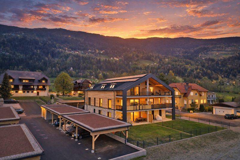 Das moderne Gebäude bei Sonnenuntergang, mit beleuchteten Innenräumen und dramatischer Himmelsfärbung über den Bergen.