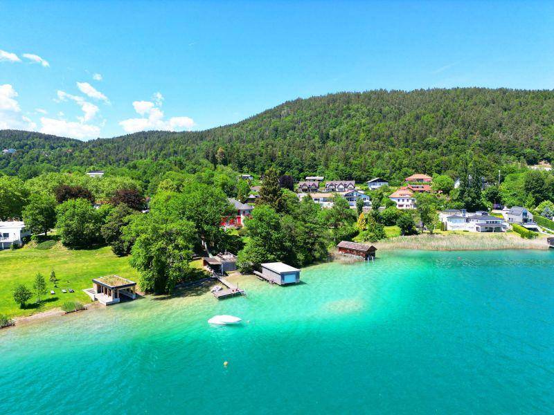 Luftaufnahme einer malerischen Seenlandschaft mit Häusern am Ufer und bewaldeten Hügeln.