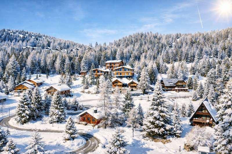 Idyllisches Bergdorf mit zahlreichen Chalets, eingebettet in eine tief verschneite Waldlandschaft unter strahlend blauem Himmel.