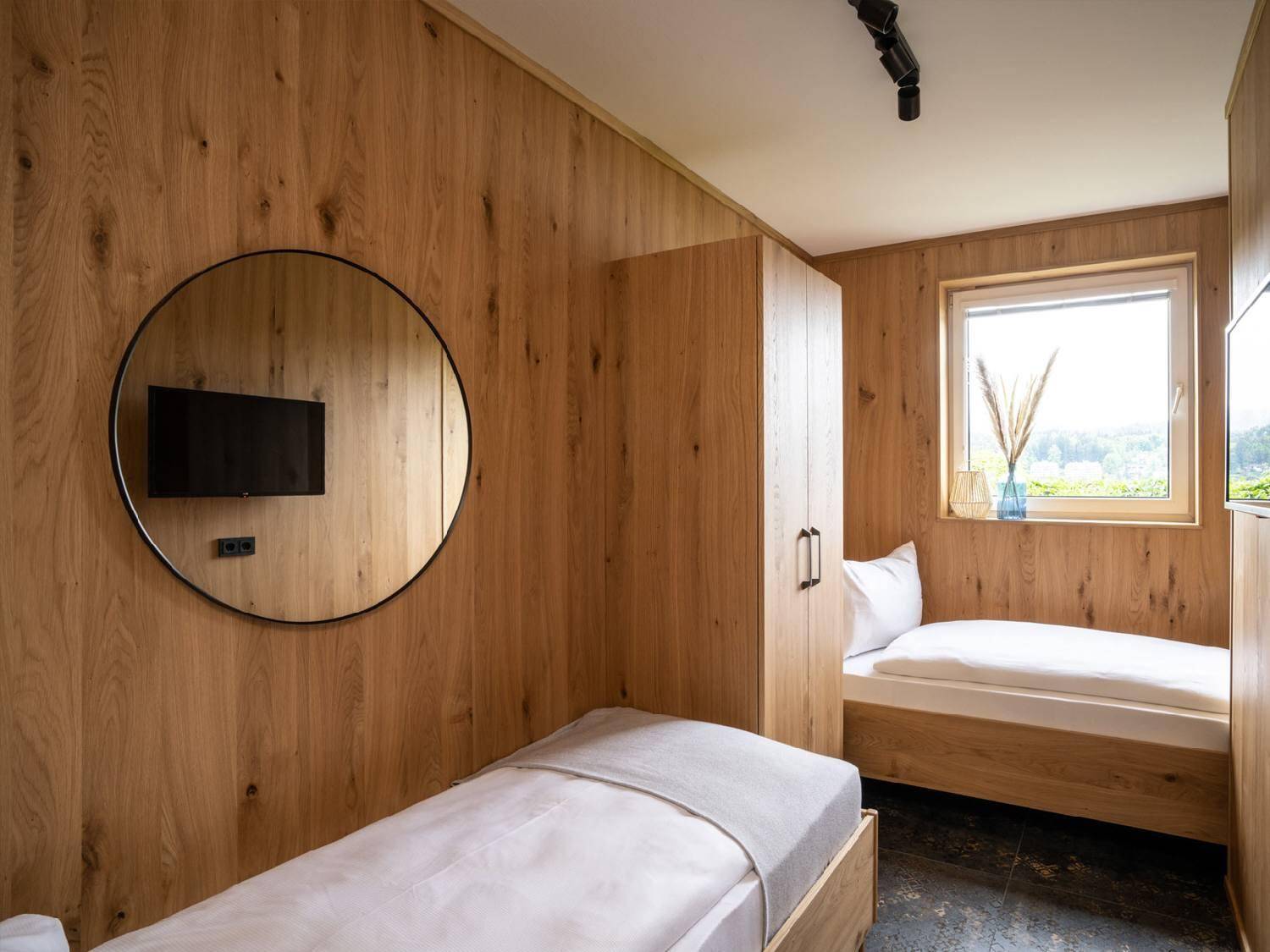 Helles Schlafzimmer mit Holzwänden, zwei Einzelbetten und einem Kleiderschrank.