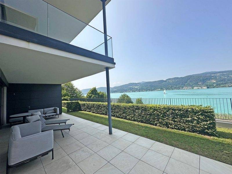 Elegante überdachte Terrasse mit Seeblick und modernen Möbeln, perfekt für Entspannung im Freien.