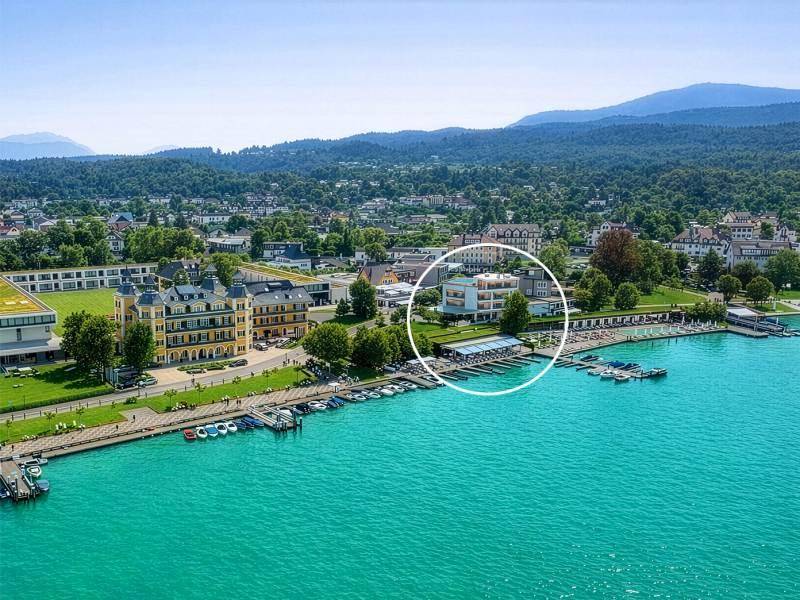 Luftaufnahme einer Stadt am See mit Bergen im Hintergrund und markiertem Gebäude.