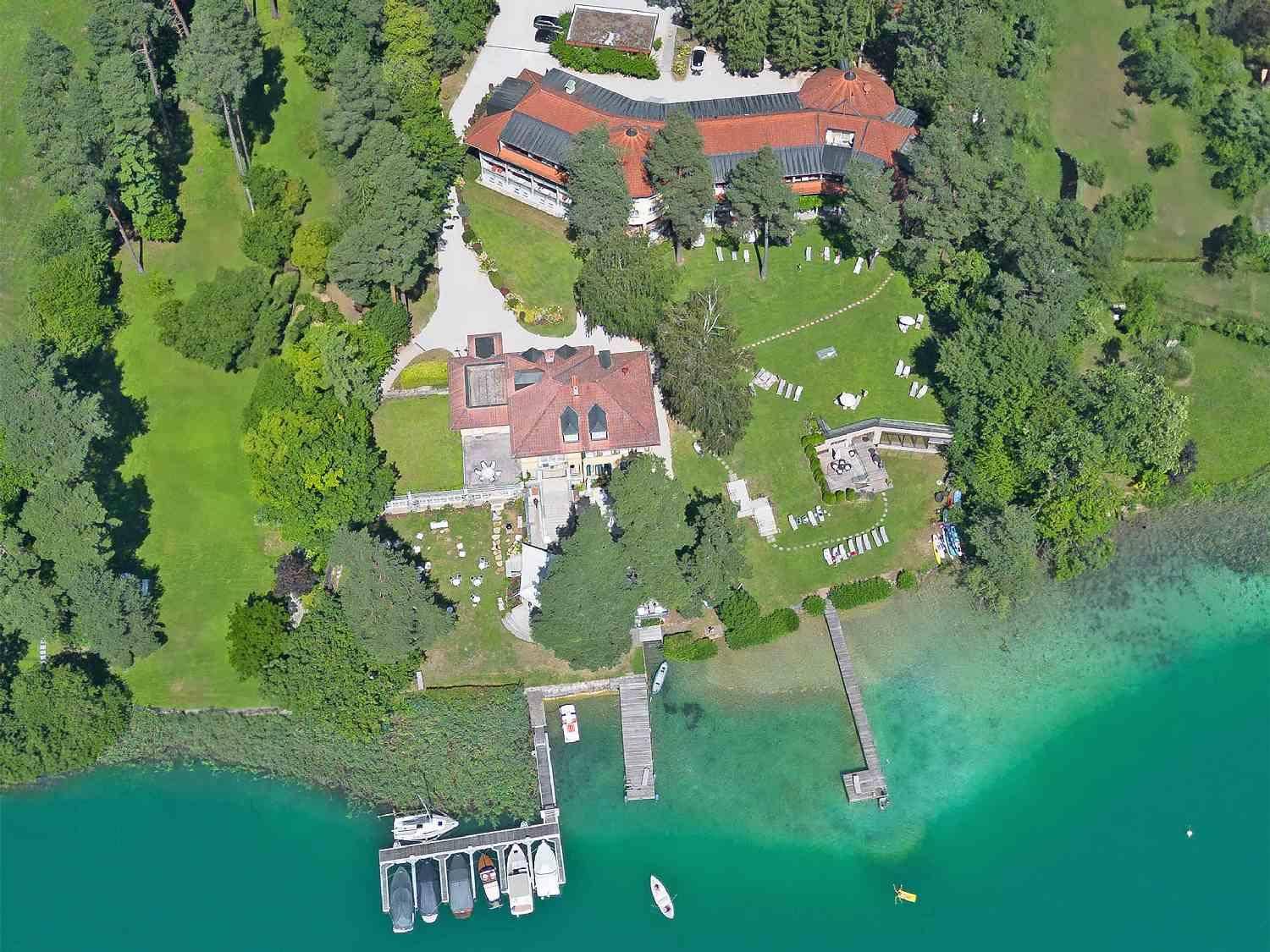 Weitläufige Luftaufnahme des Anwesens mit mehreren Gebäuden, großen Rasenflächen und Bootsanlegestellen am See.