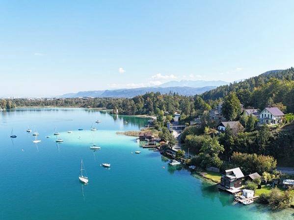 Weitläufiger Blick über den See mit Segelbooten und den bewaldeten Ufern.
