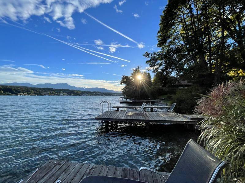 Sonniger Holzsteg am See mit Liegestühlen und weitem Blick auf die Berge und das Wasser.
