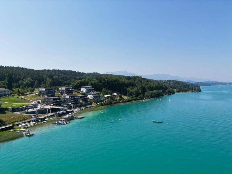Weitläufiger Blick über den See und die bewaldete Landschaft mit der modernen Wohnanlage am Ufer.