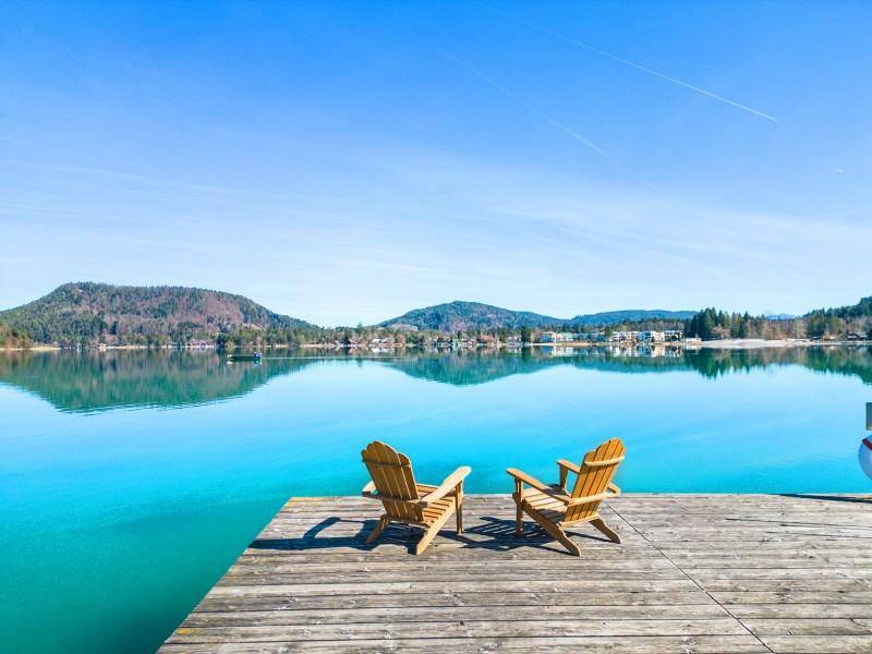 Idyllischer Holzsteg mit zwei Adirondack-Stühlen bietet einen atemberaubenden Blick auf den klaren See und die umliegenden Berge.