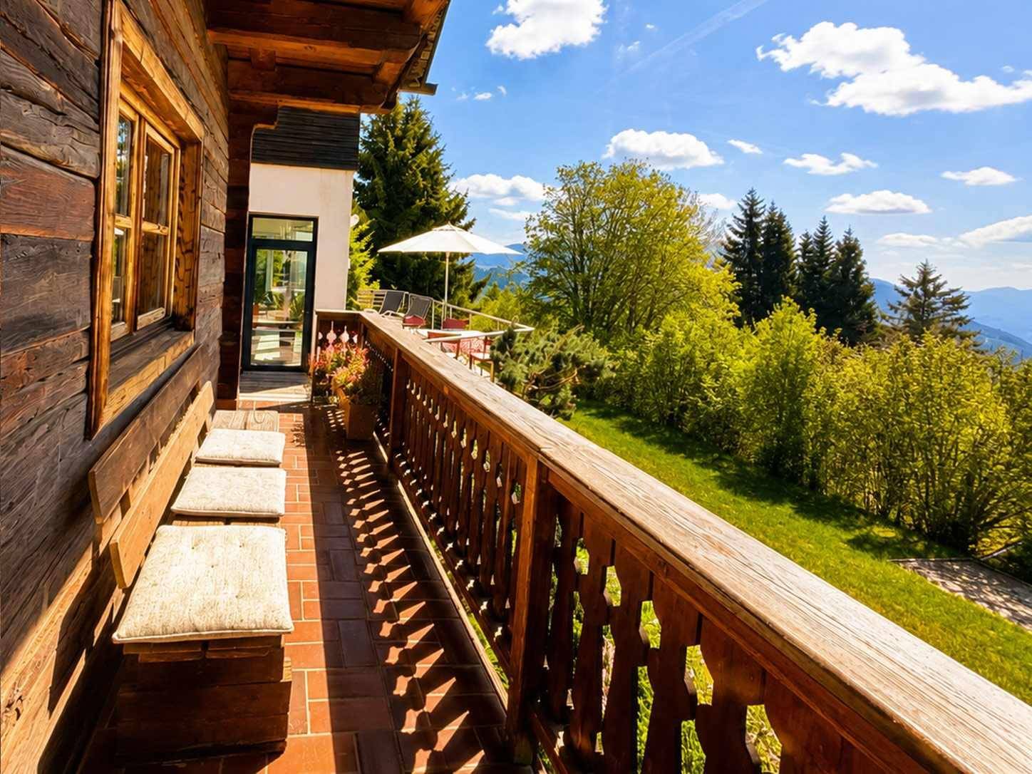 Langer Holzbalkon mit traditionellem Geländer und Sitzgelegenheiten, bietet einen weiten Blick ins Grüne.