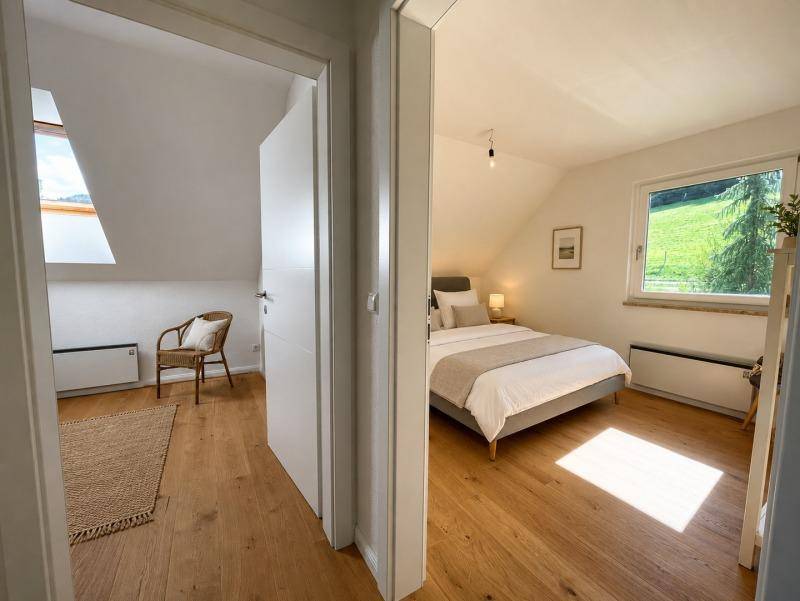 Helles Schlafzimmer mit Holzboden und Blick auf die grüne Landschaft, angrenzend an einen weiteren Raum.