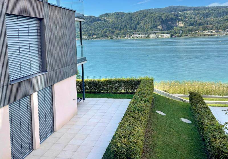 Moderne Gebäudefassade mit großen Fenstern, Terrasse und Blick auf den See und die Natur.