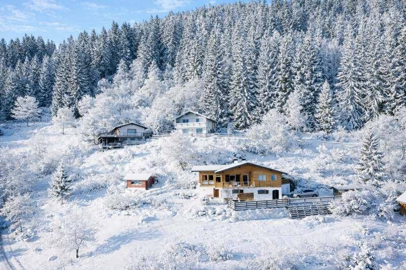 Mehrere Häuser eingebettet in eine verschneite Waldlandschaft mit majestätischem Bergpanorama.