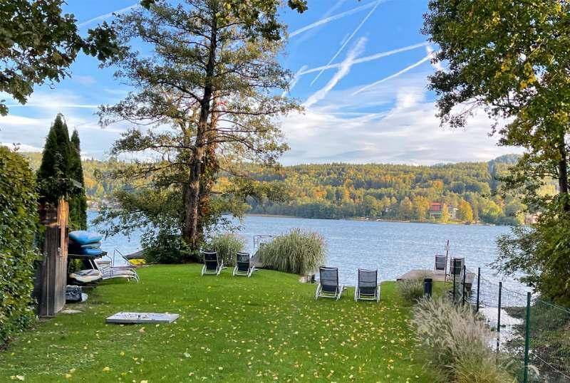 Weitläufiger Gartenbereich mit Rasen, Liegestühlen und privatem Zugang zum See mit Holzsteg.
