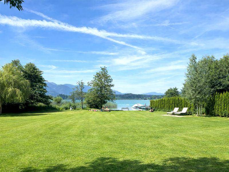 Großer Rasenbereich mit direktem Zugang zum See, umgeben von Bäumen und mit Liegestühlen zum Entspannen.