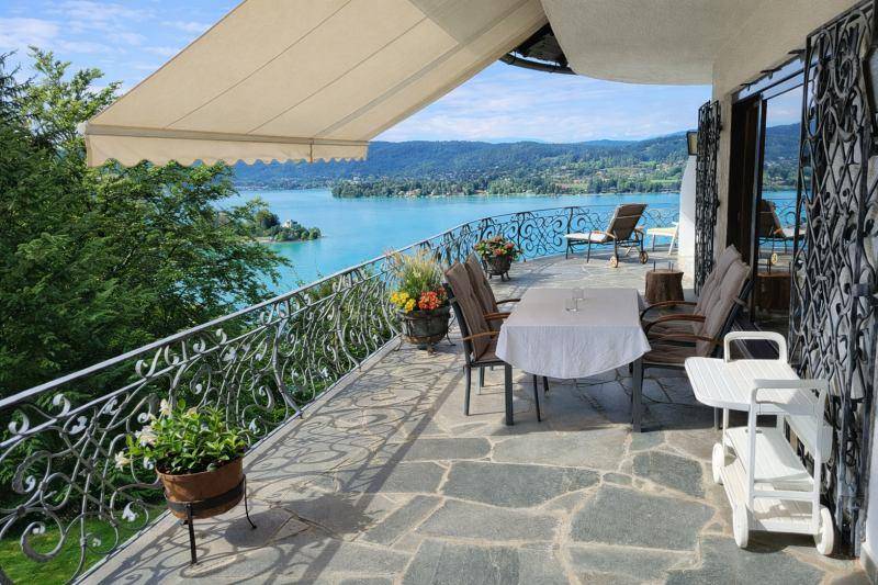 Geräumige Terrasse mit Steinfliesen, Markise und Essbereich, bietet einen weiten Blick auf den See.