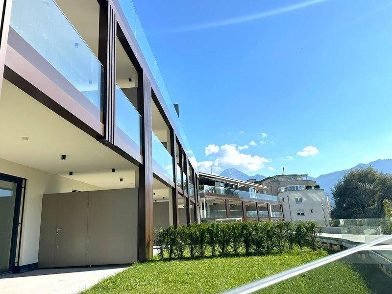 Moderne Architektur mit eleganten Glasbalkonen und gepflegter Grünfläche vor einer Bergkulisse.