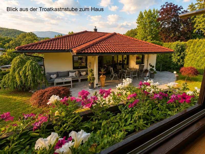 Blick auf das Haus und den blühenden Garten mit Terrasse bei Sonnenuntergang.