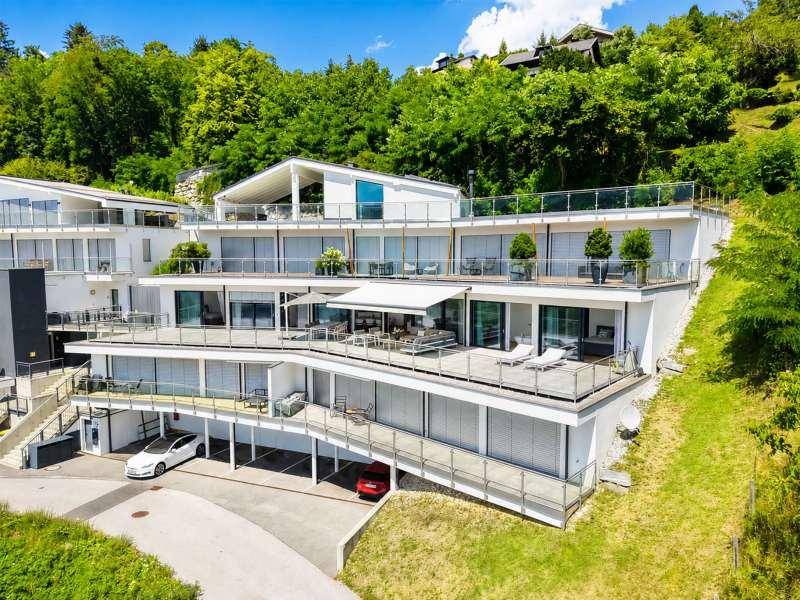 Moderne Terrassenhäuser in Hanglage mit mehreren Ebenen, großen Glasfronten und Panoramablick auf die Umgebung.