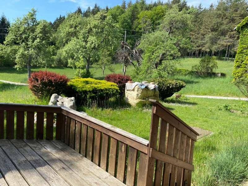 Holzterrasse mit Geländer und Blick auf einen gepflegten Gartenbereich mit Sträuchern und Felsen.