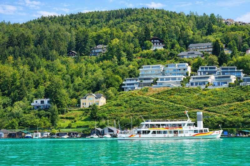 Malerischer Blick auf den See mit Häusern am bewaldeten Hang und einem Ausflugsschiff.