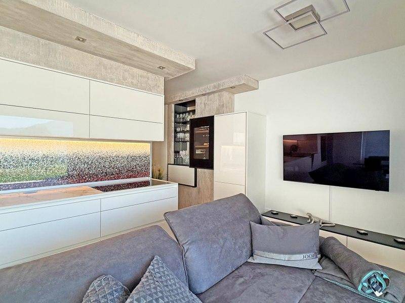 Moderner Wohnbereich mit grauem Sofa, Wandfernseher und integrierter Küche mit Weinkühler.