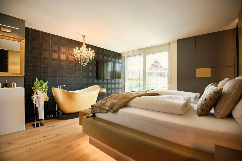 Modernes Schlafzimmer mit freistehender Badewanne, Holzboden und stilvoller Beleuchtung.