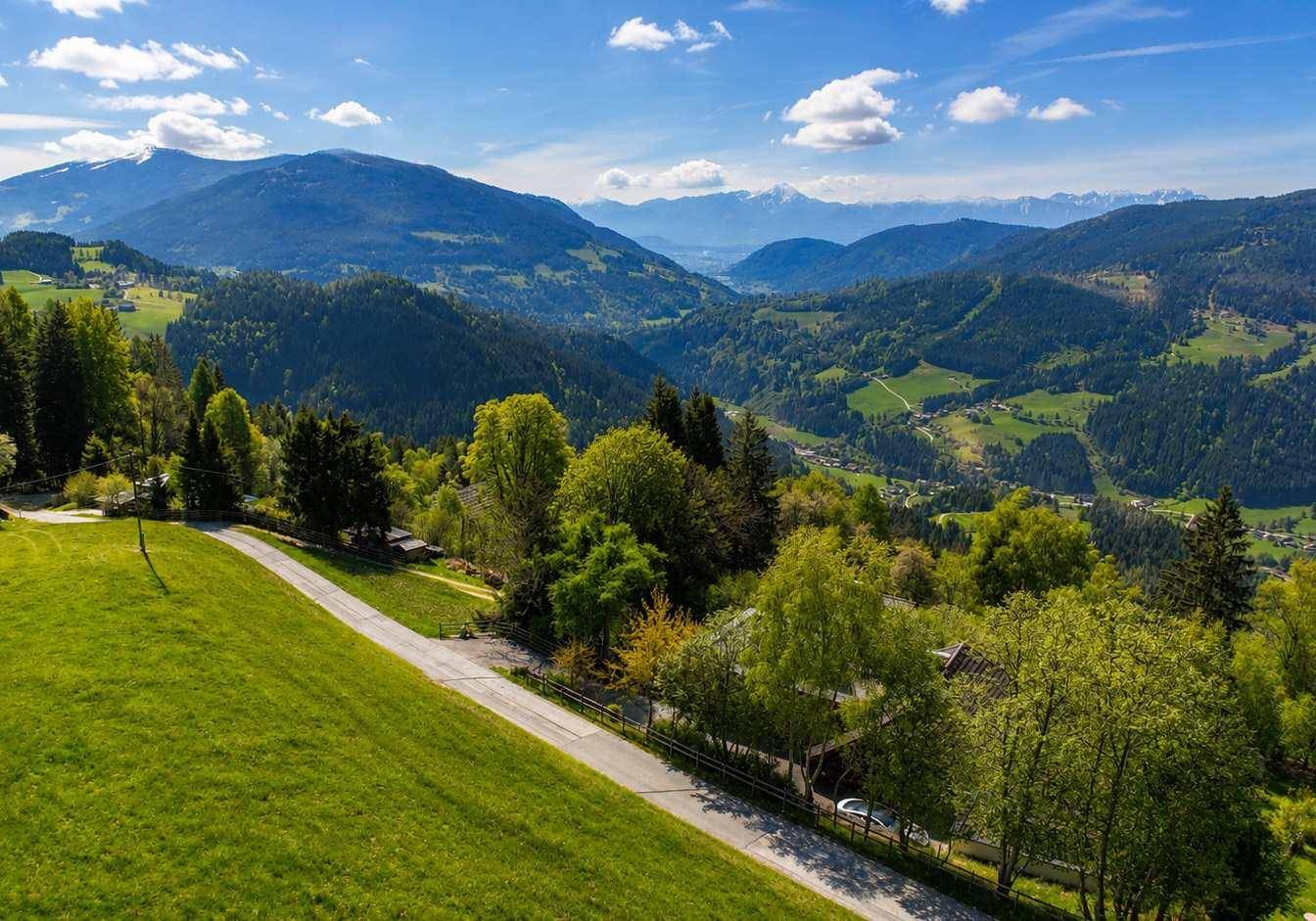 Panoramablick aus der Vogelperspektive auf die weitläufige grüne Berglandschaft mit verstreuten Häusern.