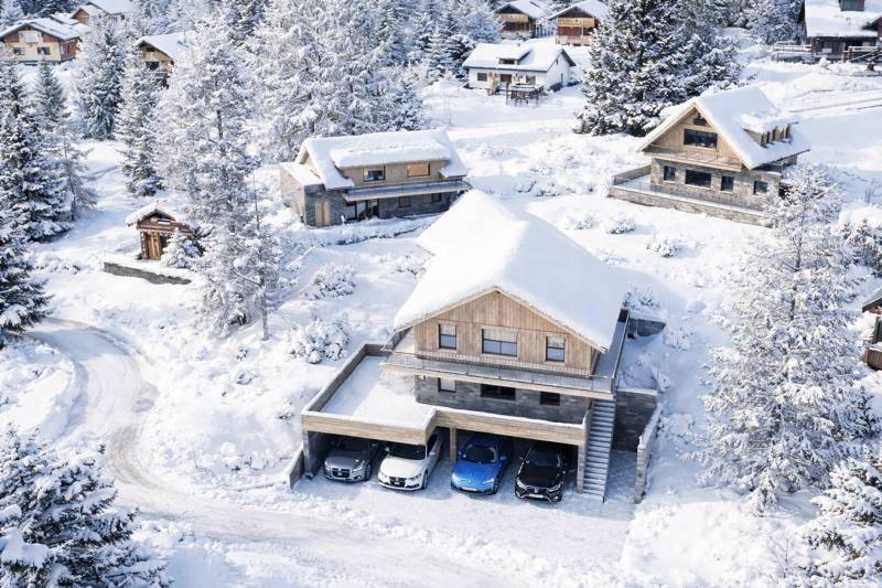 Luftaufnahme von modernen Chalets in einer verschneiten Bergregion mit integrierten Garagen und umliegenden Wäldern.