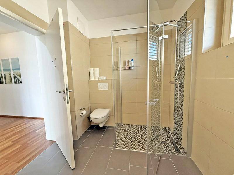 Modernes Badezimmer mit wandmontierter Toilette und geräumiger Duschkabine.