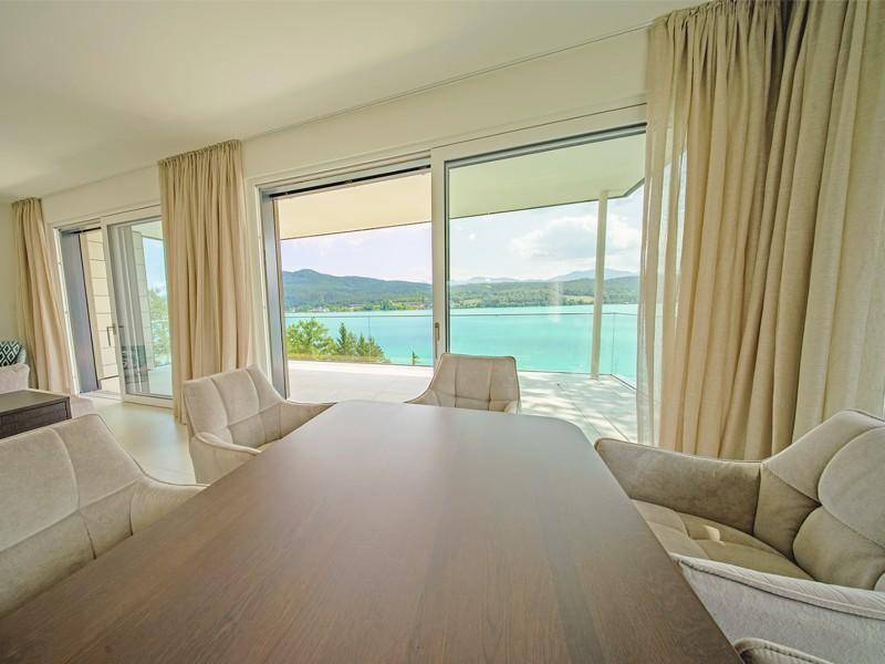 Eleganter Essbereich mit großem Holztisch, bequemen Stühlen und Panoramafenstern mit Seeblick.