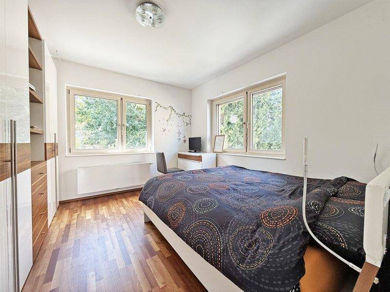 Helles Schlafzimmer mit Holzboden, großen Fenstern und Blick ins Grüne.