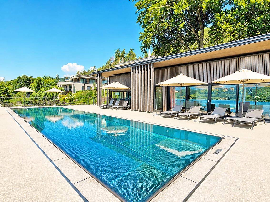 Moderner Poolbereich mit Holzfassade und großen Fenstern, die einen weiten Blick auf den See bieten.