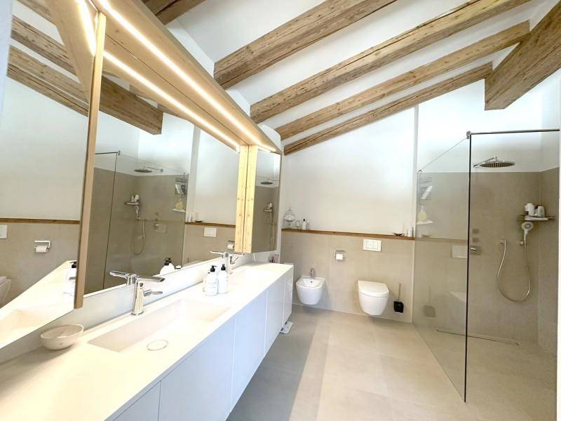 Modernes Badezimmer mit Doppelwaschbecken, begehbarer Dusche und Holzbalken an der Decke.