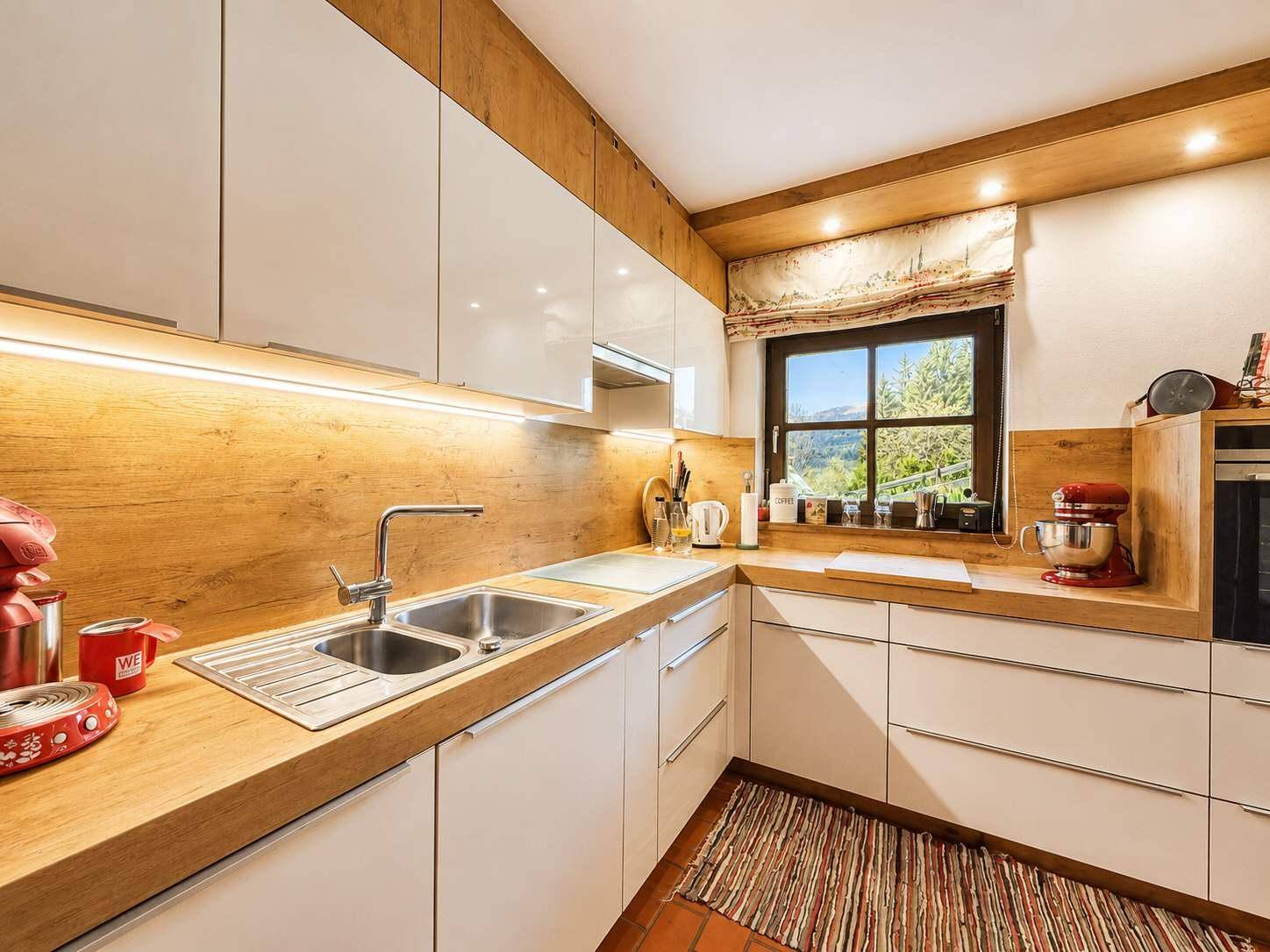 Moderne Küche mit weißen Hochglanzfronten, Holzarbeitsplatten und Blick auf die Berge.