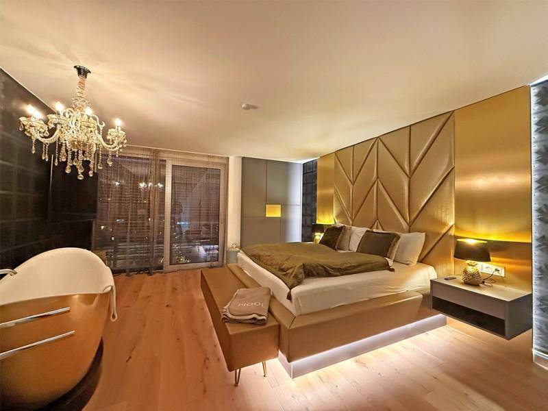 Elegantes Schlafzimmer mit freistehender Badewanne, gepolsterter Wand und indirekter Beleuchtung.