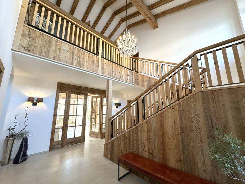 Beeindruckende Eingangshalle mit offener Holztreppe, hohen Decken und einem eleganten Kronleuchter.